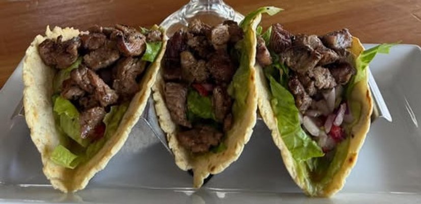 Three beef tacos with lettuce and toppings on white plate